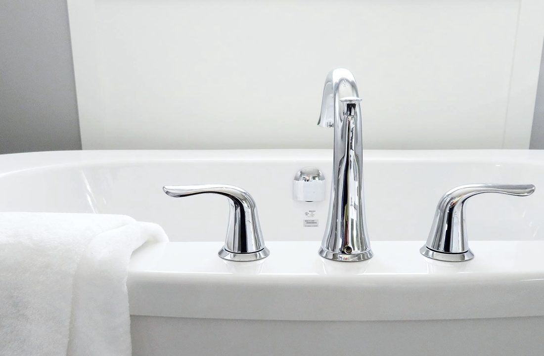 The corner of a bath with chrome taps and a folded white towel